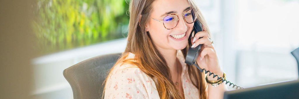 R&eacute;ceptionniste souriante du BLSI r&eacute;pondant au t&eacute;l&eacute;phone derri&egrave;re le comptoir d&rsquo;accueil