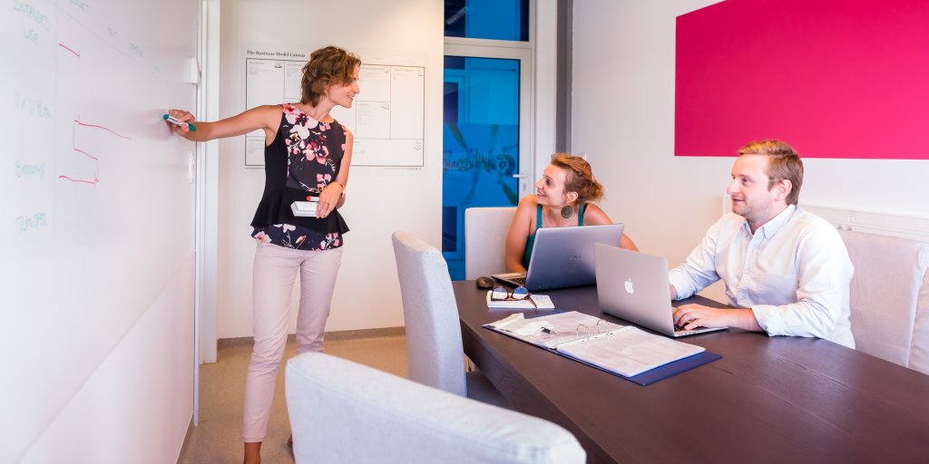 S&eacute;ance de coaching strat&eacute;gique au BLSI avec une coach pr&eacute;sentant un plan sur un tableau blanc &agrave; deux entrepreneurs
