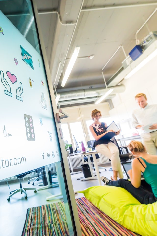 Une entrepreneure consulte un document pendant qu&rsquo;une coach anime une s&eacute;ance de travail devant un paperboard