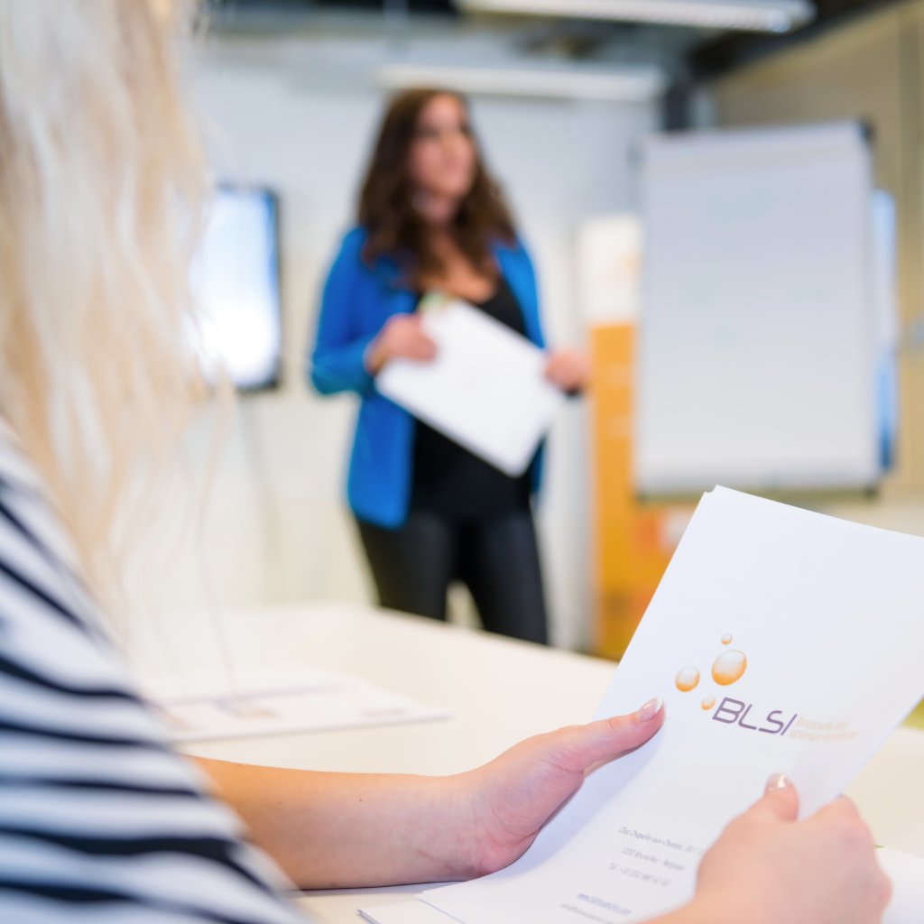 Une entrepreneure consulte un document pendant qu&rsquo;une coach anime une s&eacute;ance de travail devant un paperboard